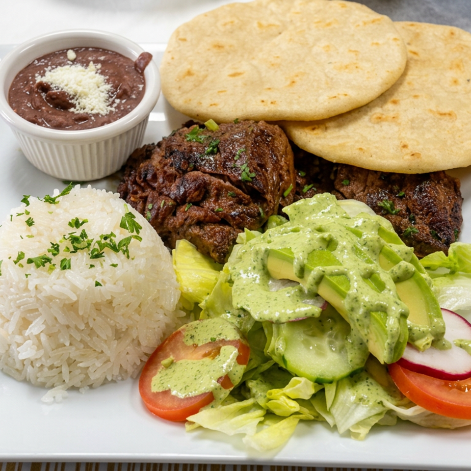 Plate of grilled beef, white rice, beans, flatbreads, and salad topped with creamy green sauce.