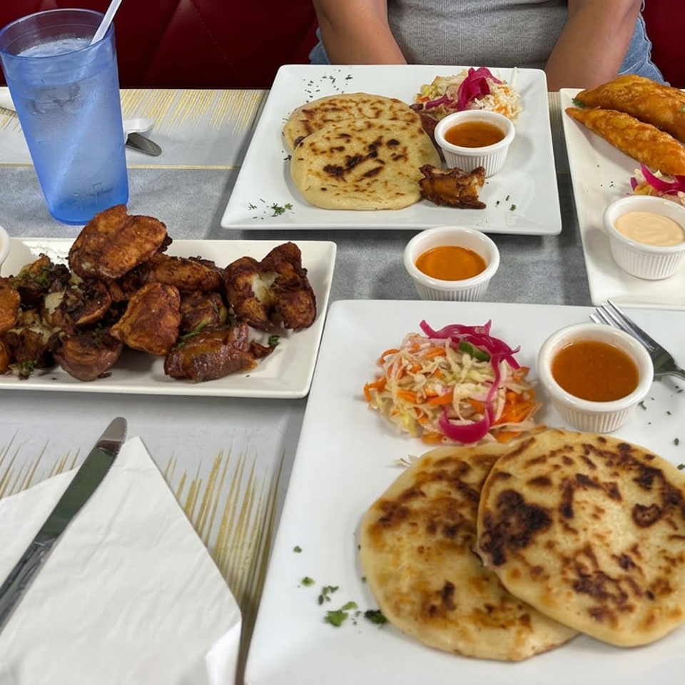 Restaurant table spread with grilled flatbreads, fried chicken, savory pastries, colorful slaw, dipping sauces, and a blue drink.